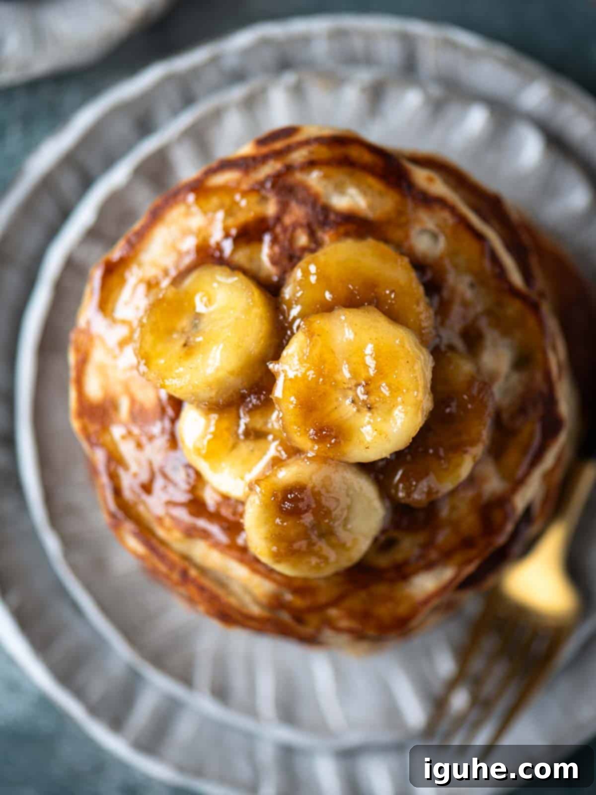 Homemade Banana Bread Pancakes with Banana Compote 3 An overhead close-up shot of a stack of fluffy banana bread pancakes generously drizzled with rich, golden banana compote, highlighting the vibrant colors and appealing texture of the dish.