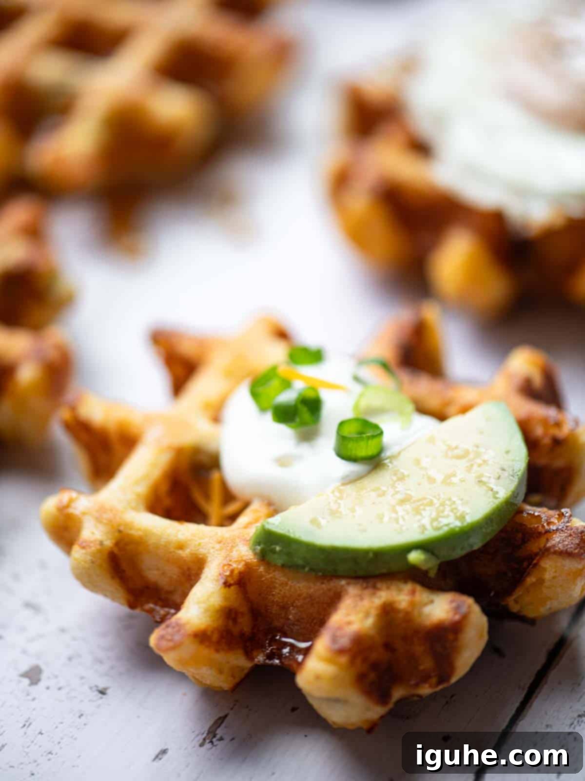 Zesty Cheddar Chili Waffles 6 Close up of a waffle with sour cream and sliced avocado on top.