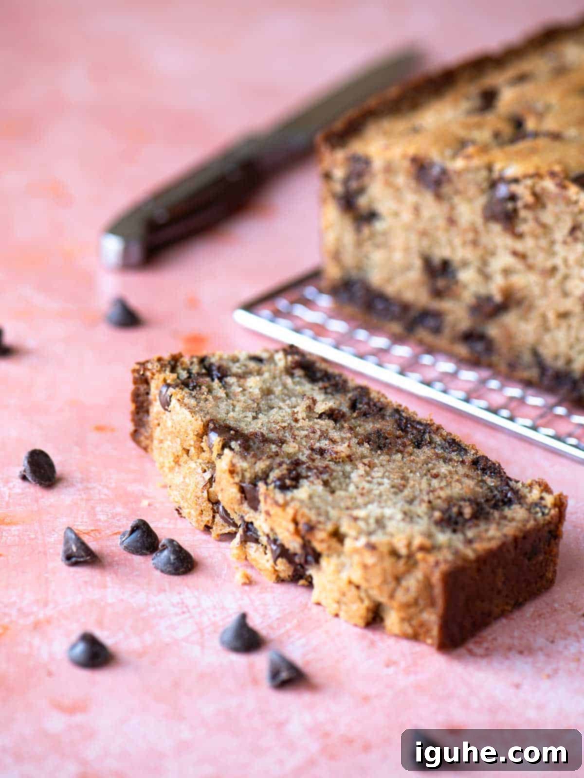 Golden Chocolate Chip Loaf 2 Eye level slice of chocolate chip loaf on a pink surface.