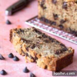 Irresistible Chocolate Chip Loaf Cake 12 Slice of chocolate chip cake on a pink surface with chips in the background.