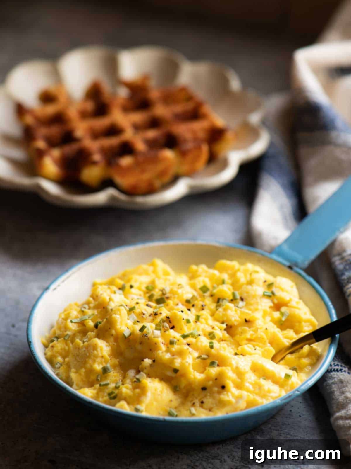 The Ultimate Buttermilk Scramble 8 Scrambled eggs in a blue skillet with a waffle in the background.
