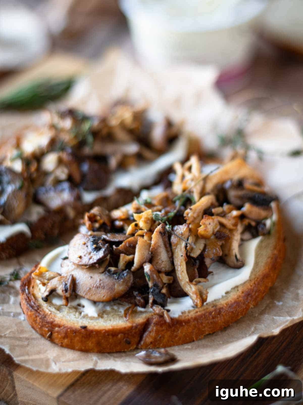 Rustic Wild Mushroom Toast 8 Angled view of 2 slices of mushroom tartine on parchment paper.