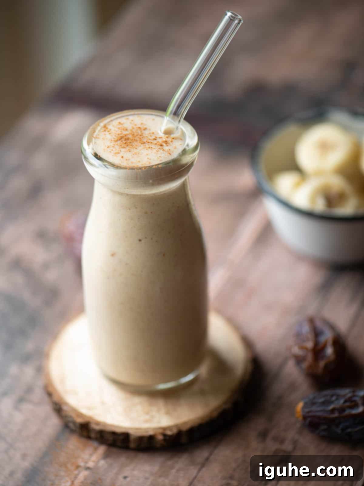 Velvet Banana Date Delight 3 Angled view of a banana smoothie with a straw in it.