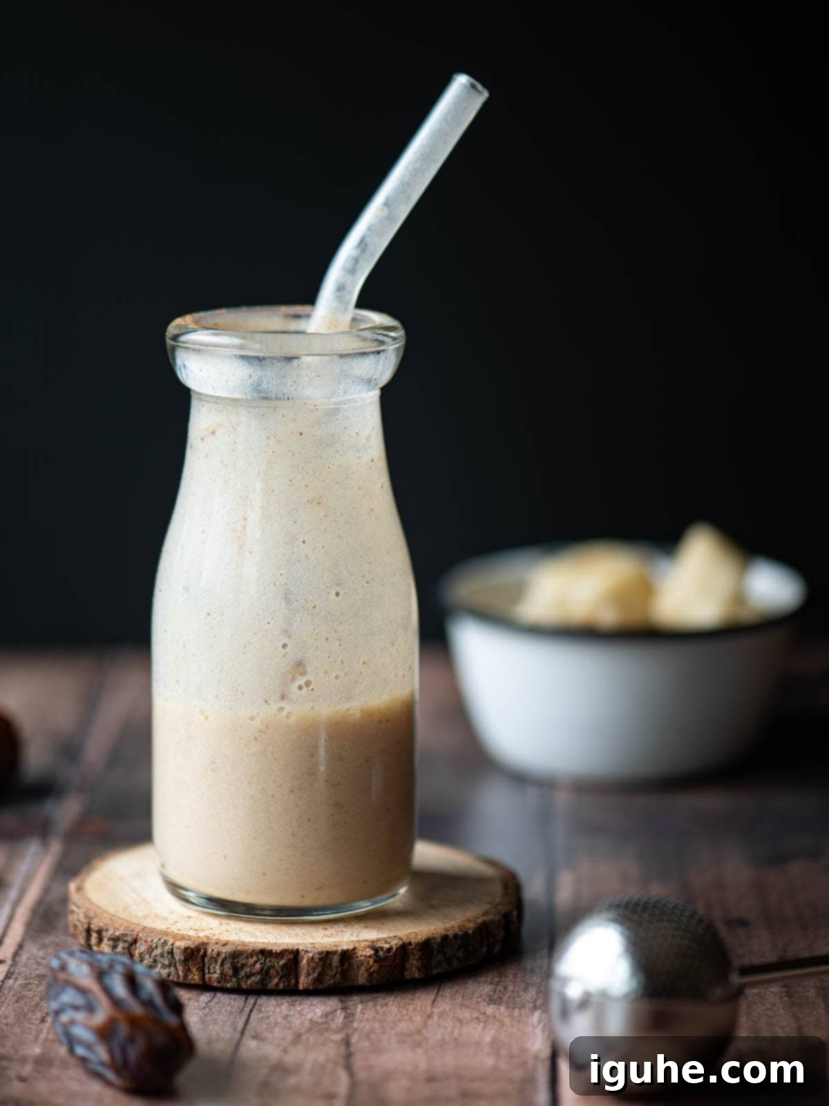 Velvet Banana Date Delight 6 Half drunk smoothie in a clear jug on a wood surface.