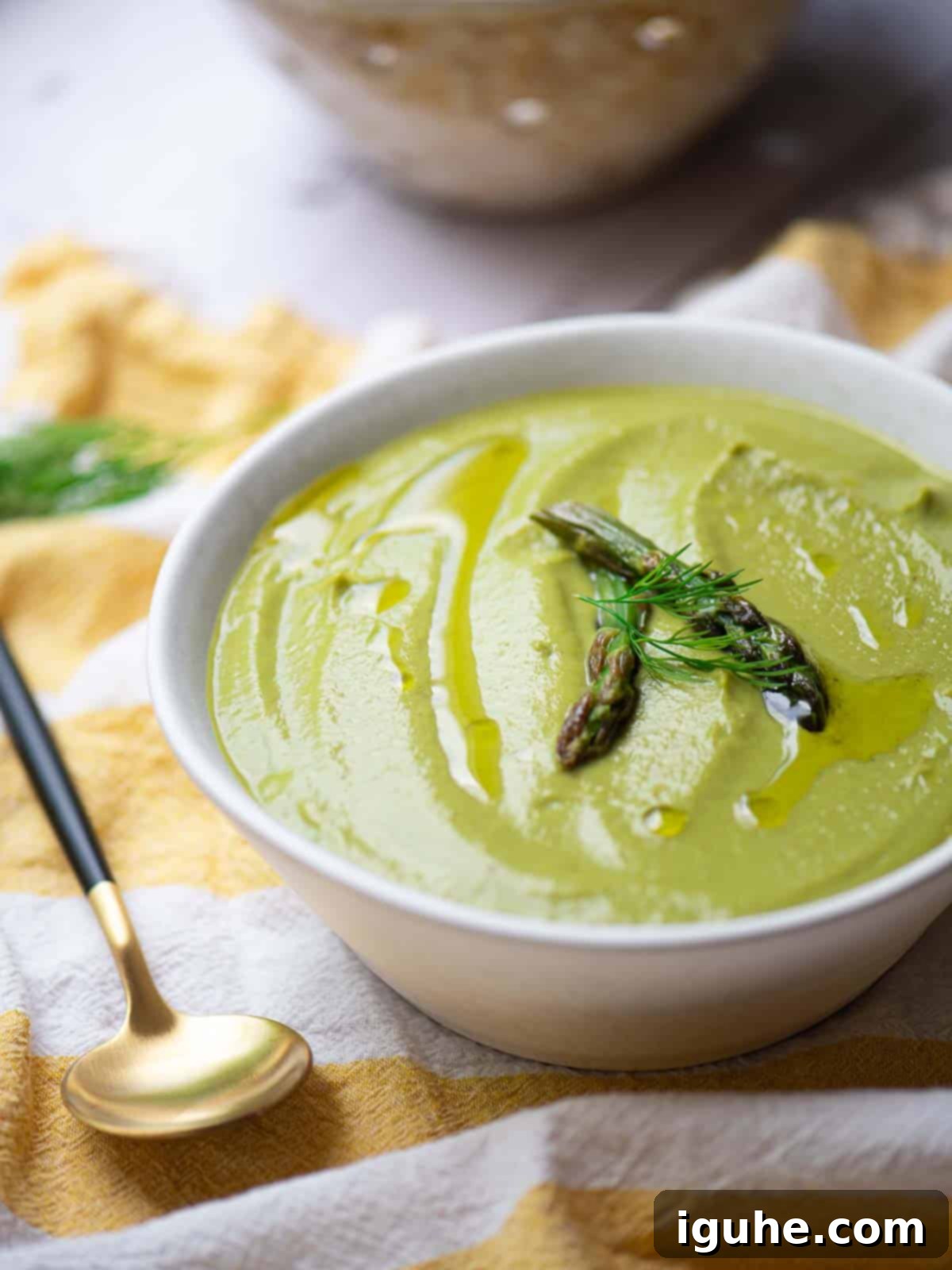Close up of asparagus leek soup in a white bowl over a yellow striped linen.