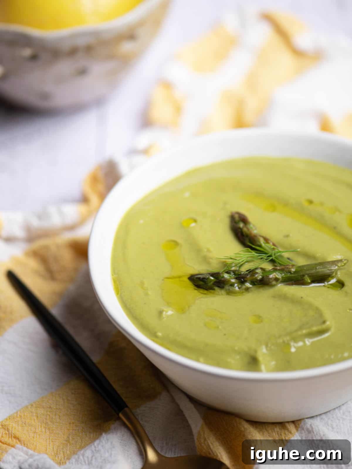 Velvety Asparagus Leek Soup 6 Angled view of asparagus soup in a white bowl with a lemon in the background.