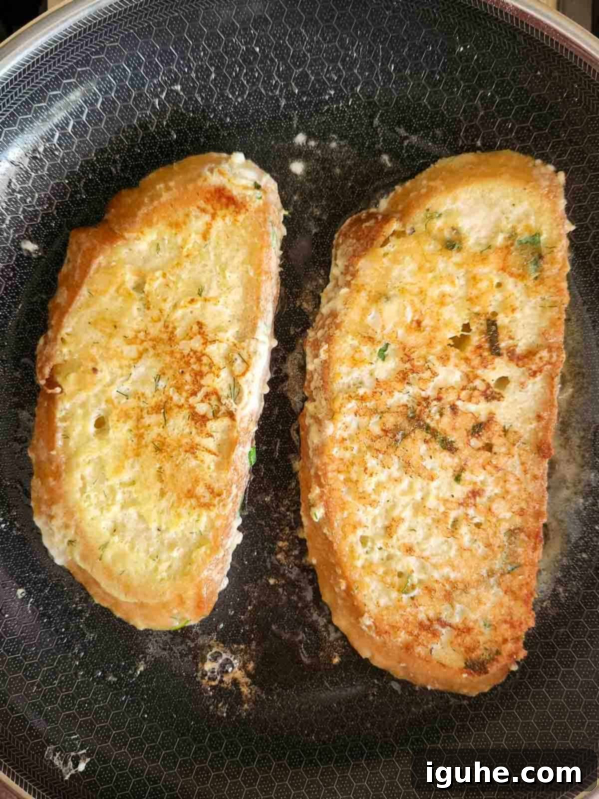 Parmesan, Lemon and Herb Savory French Toast 9 Two slices of French toast in a pan being showing the browned cooked side.