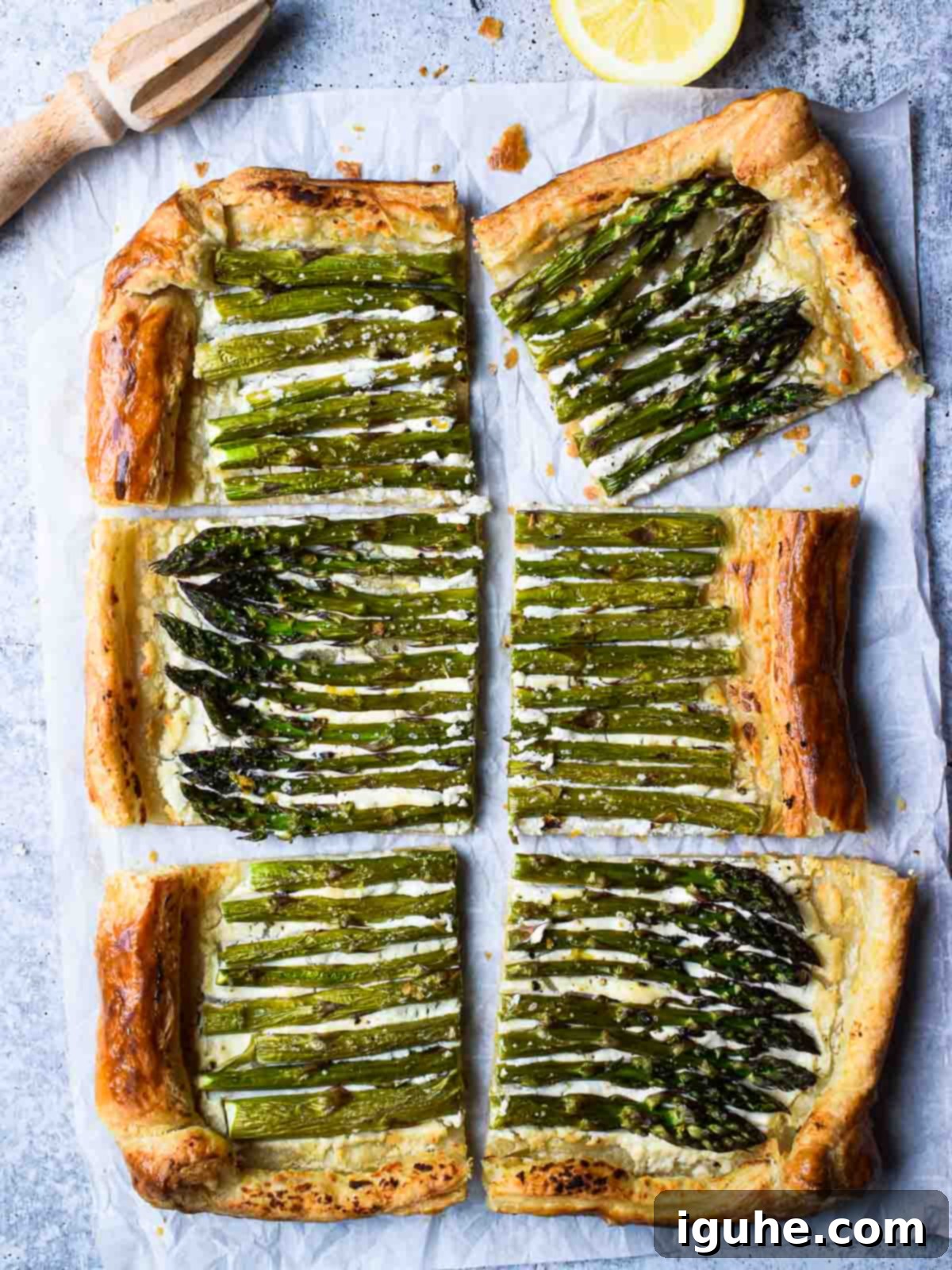 Overhead of asparagus and whipped goat cheese puff pastry tart cut into six pieces with a lemon to the side