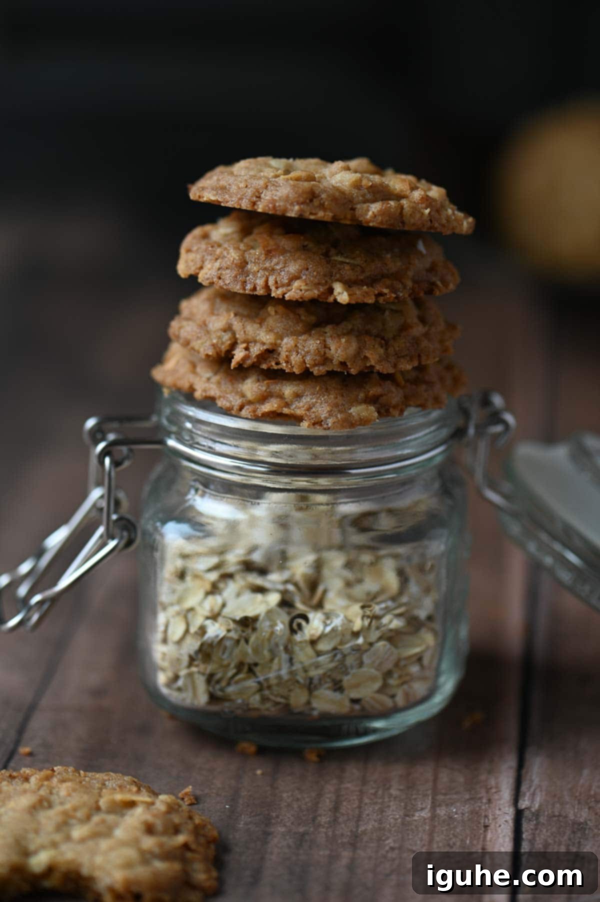 A charming stack of freshly baked coconut oatmeal cookies resting atop a Mason jar filled with rolled oats, with more loose oats scattered around.