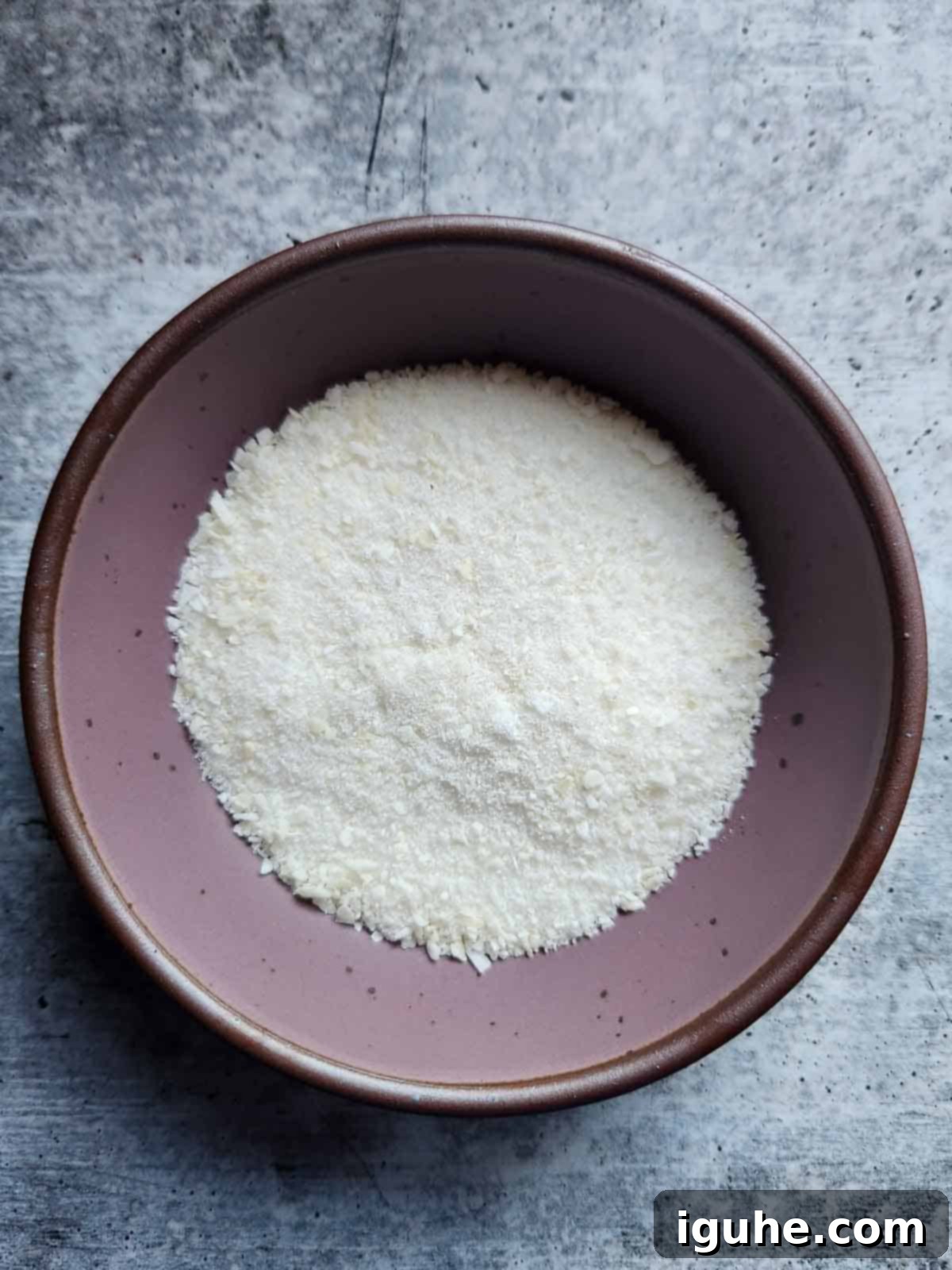 A vibrant purple bowl filled with a blend of finely ground coconut and white sugar, ready for mixing.