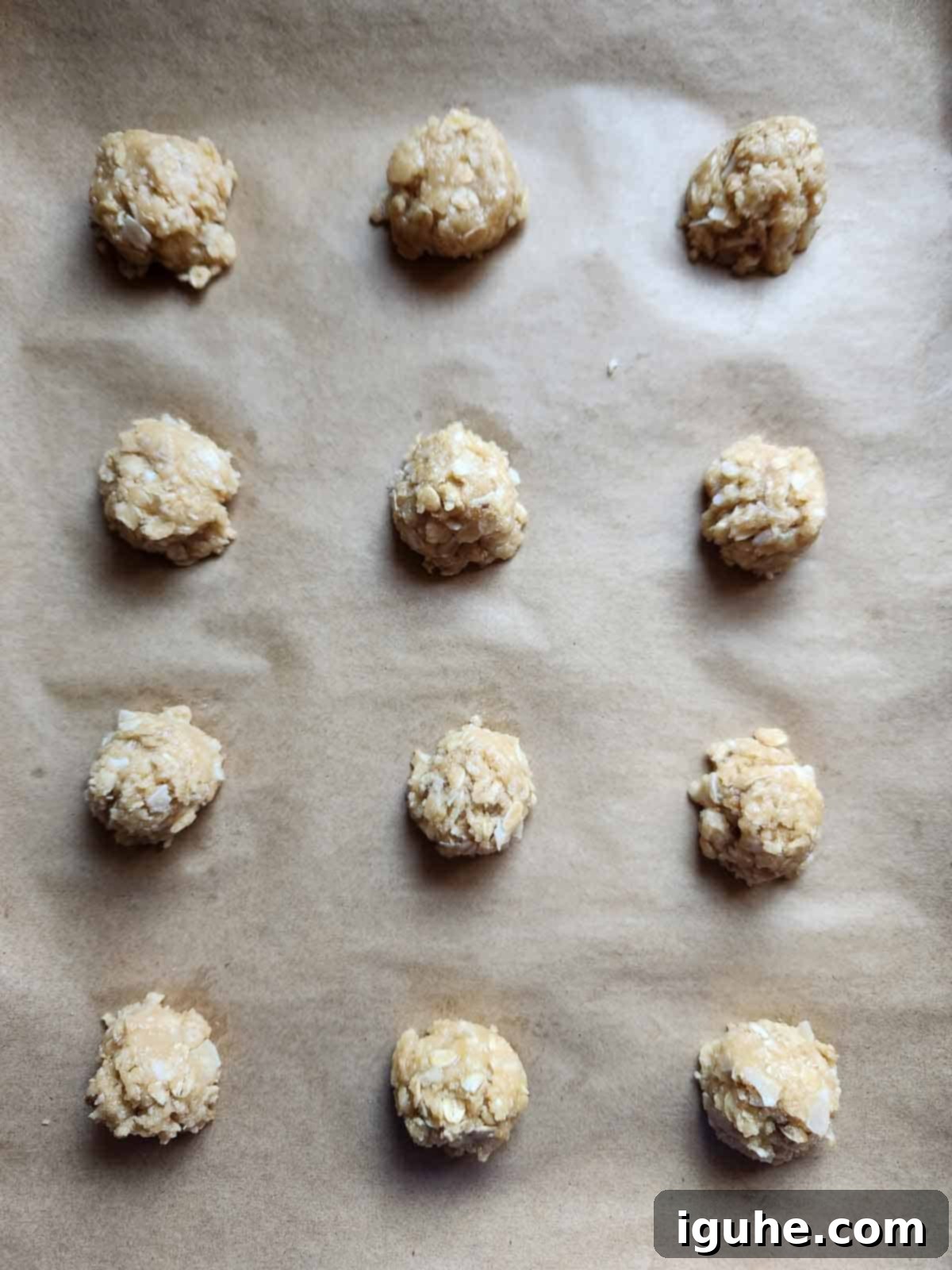 Raw coconut oatmeal cookie dough dropped in rounded mounds on a parchment-lined baking sheet, spaced for even baking.
