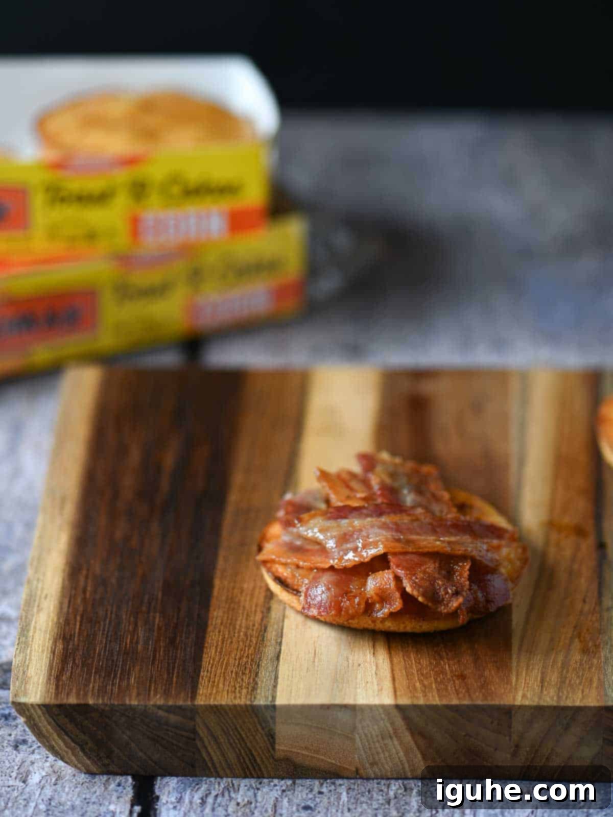 A crispy slice of bacon layered atop a buttered, golden-brown corn toaster cake, forming the first savory component of the breakfast sandwich.