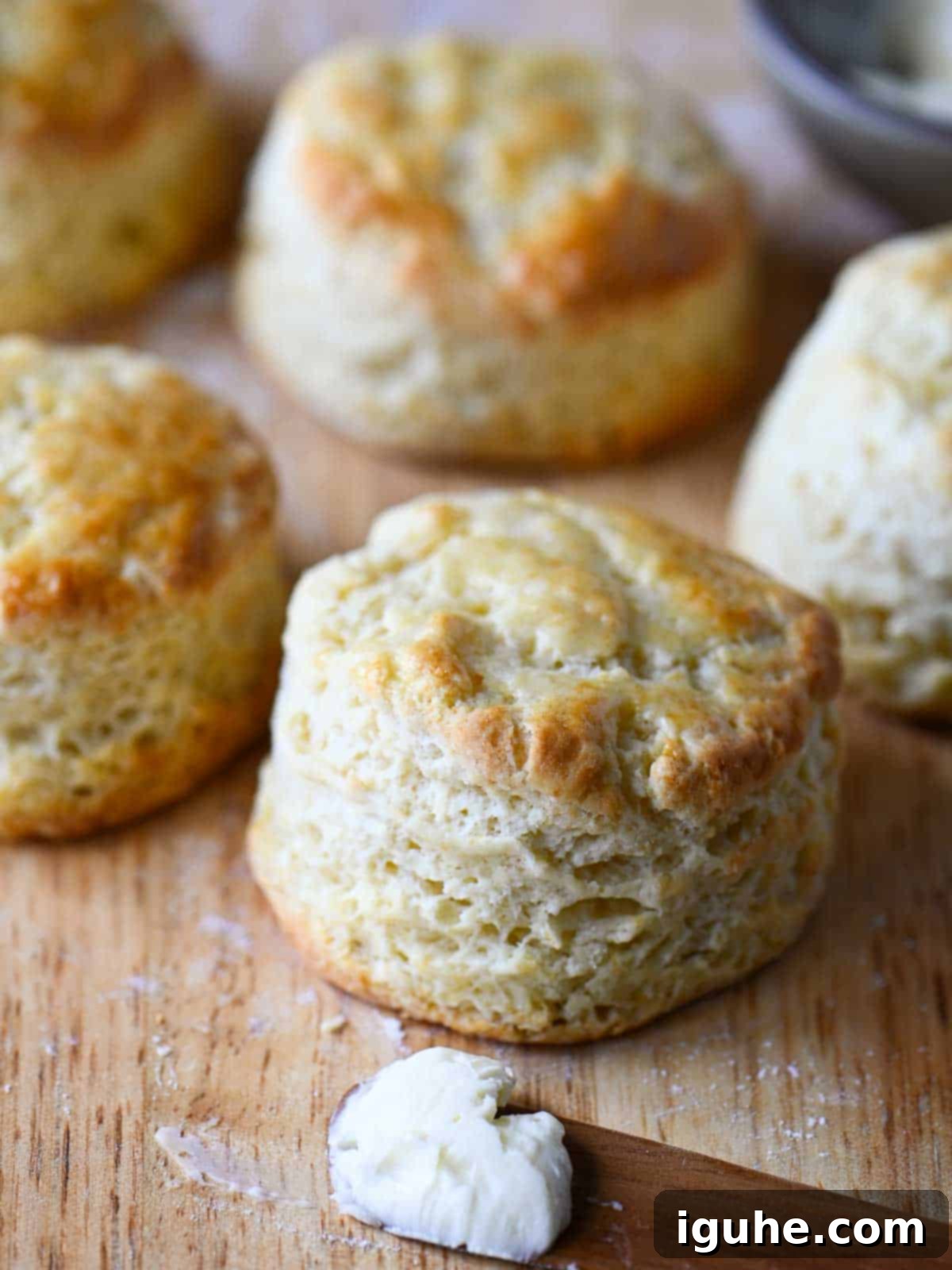 Cake Flour Biscuits 2 Golden brown cake flour biscuits on a wooden cutting board next to a knife with butter.