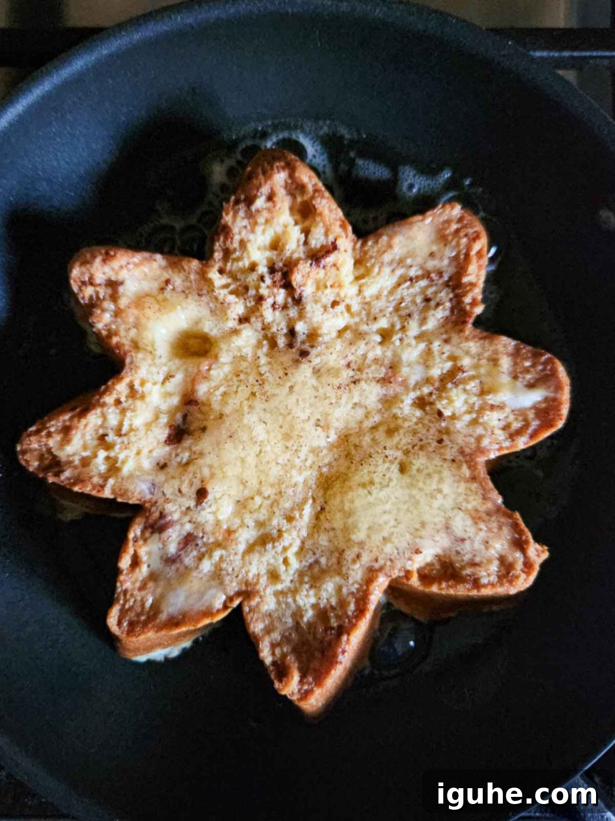 A slice of Pandoro French toast cooking in a black skillet.