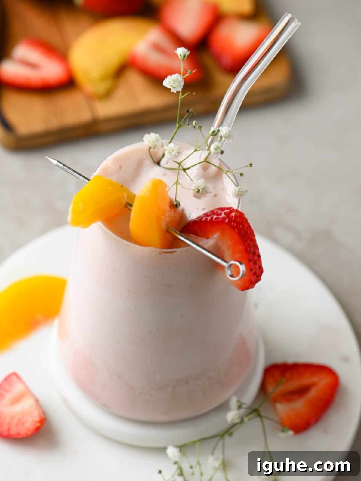 Strawberry Peach Bliss Smoothie 2 A vibrant strawberry peach smoothie in a clear glass, adorned with fresh fruit toppings.