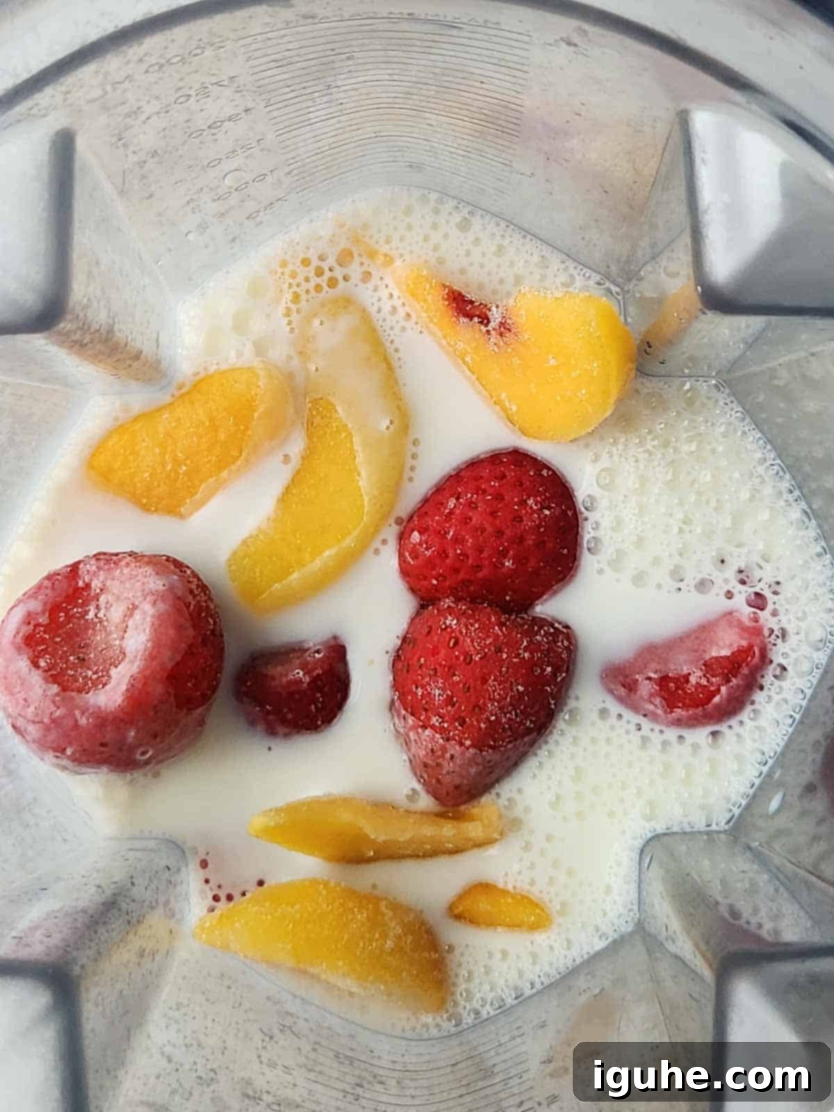 Strawberry Peach Bliss Smoothie 5 An overhead view of milk and frozen fruit inside a blender.