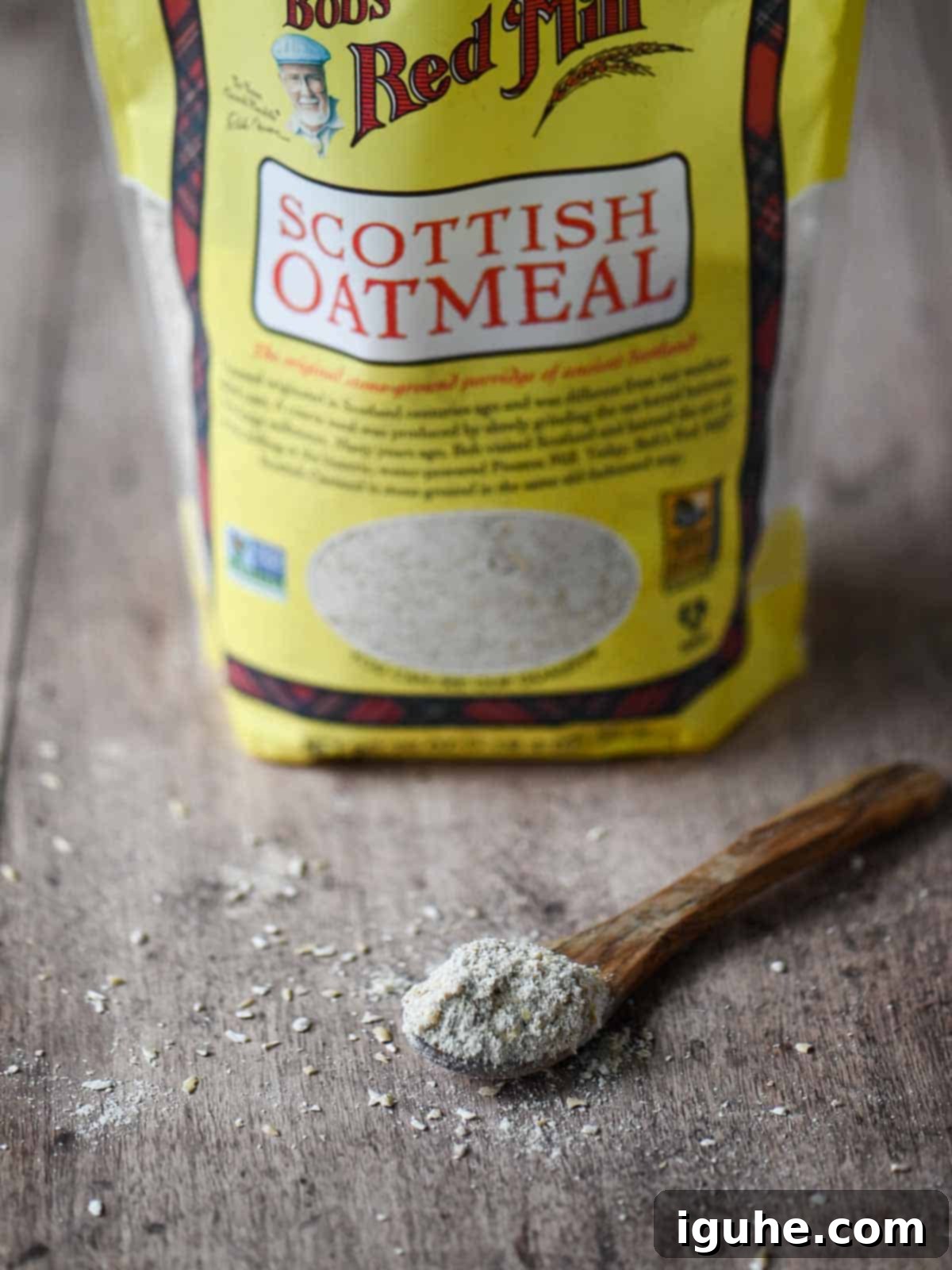 Dates and Honey: A Twist on Classic Scottish Oatmeal 3 A close-up showcasing raw Scottish oats on a wooden spoon, with a bag of Scottish oats blurred in the background.