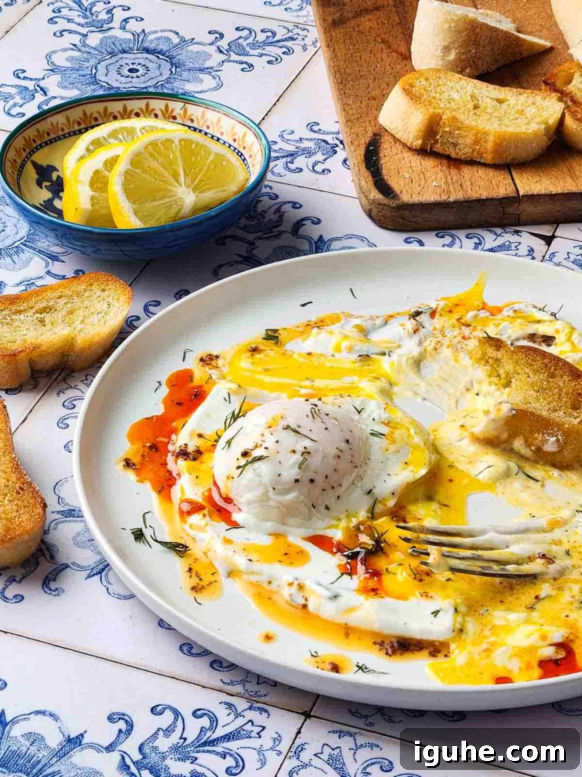 Chili Butter Poached Eggs with Garlicky Yogurt 3 A table view of chili-poached eggs half eaten, with crusty bread dunked invitingly into the egg yolk.