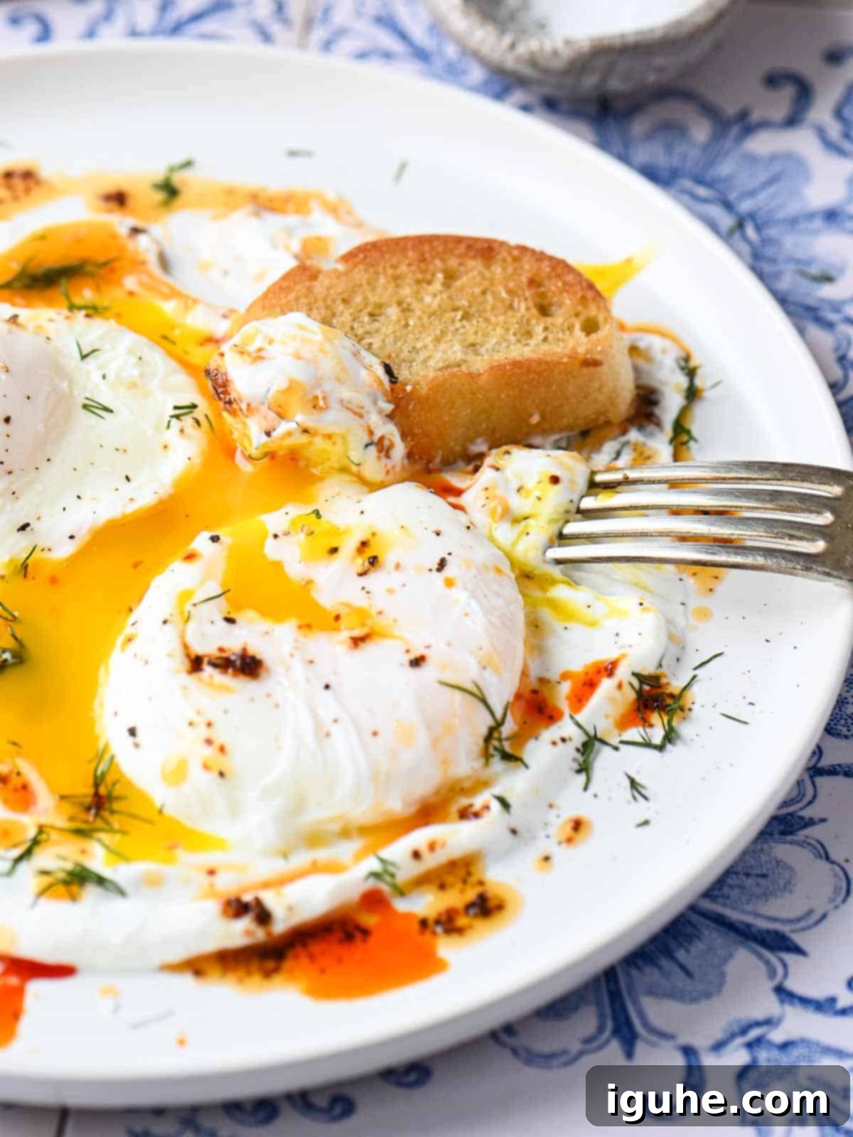 Chili Butter Poached Eggs with Garlicky Yogurt 7 Poached eggs on a white dish, presented with a side of toasted bread and a fork, ready for enjoying.