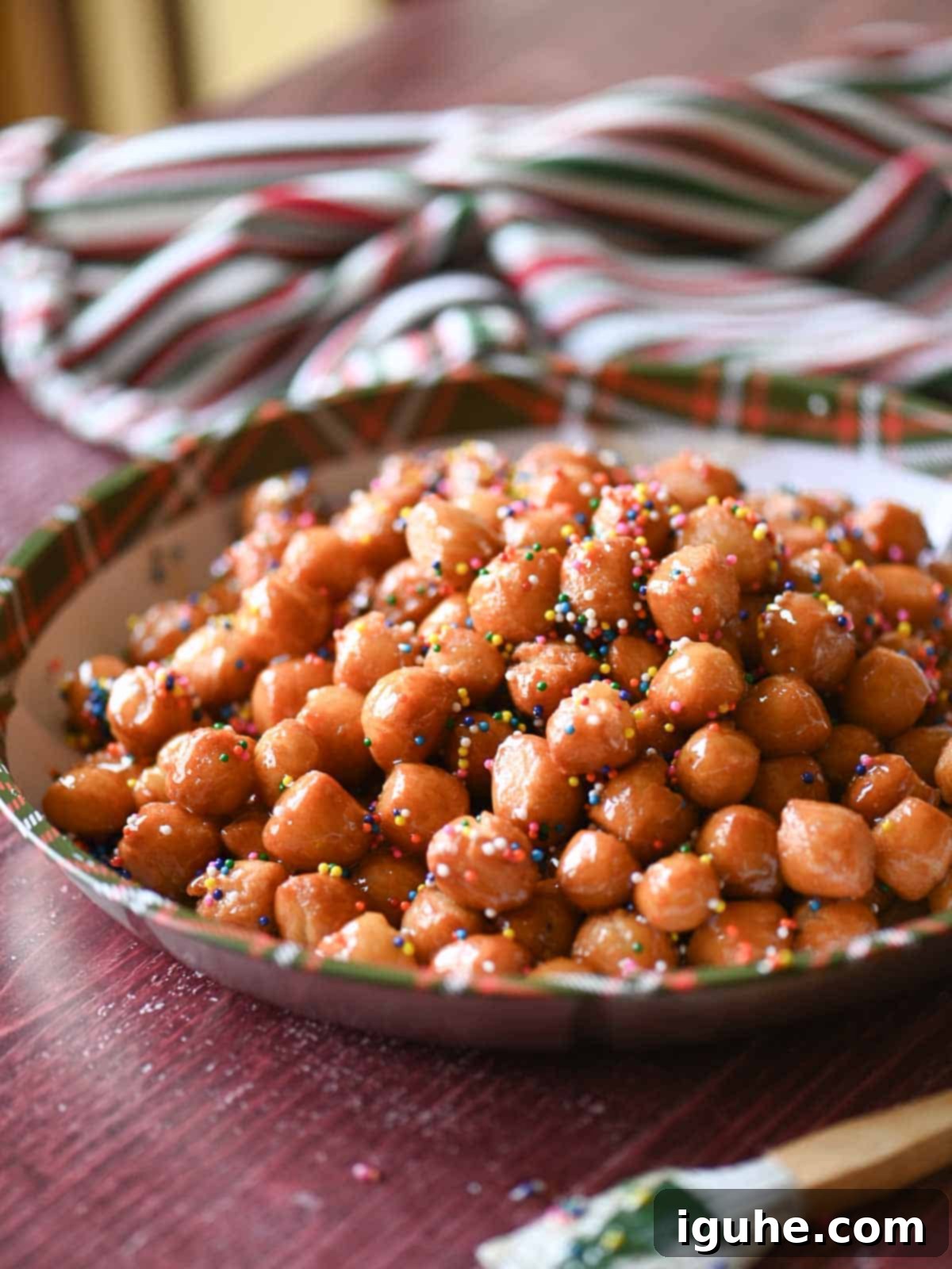 Honey-Drizzled Italian Dough Balls 9 An angled view of Italian honey balls beautifully arranged on a tray, set against a rustic red wooden surface.