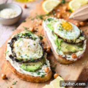 Two hummus toasts on a cutting board with eggs and avocado.