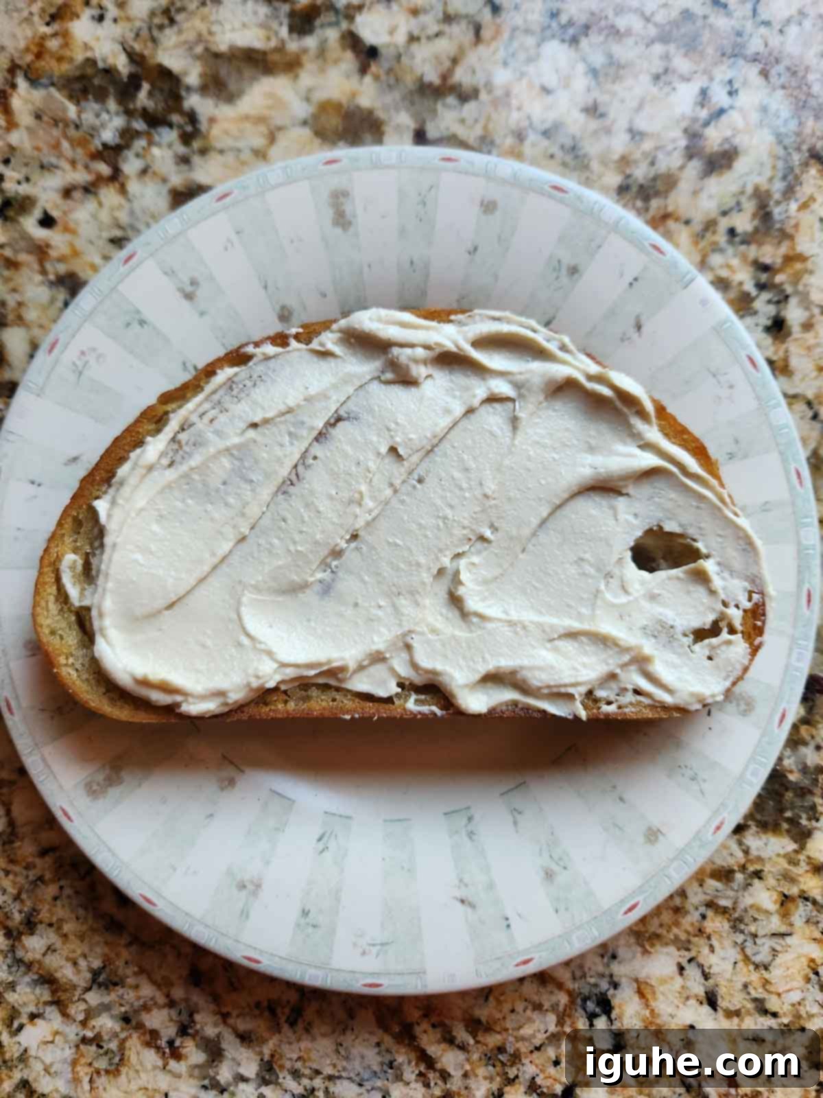 Creamy hummus artfully spread on a slice of golden-brown toast, ready to be topped with flavorful ingredients.