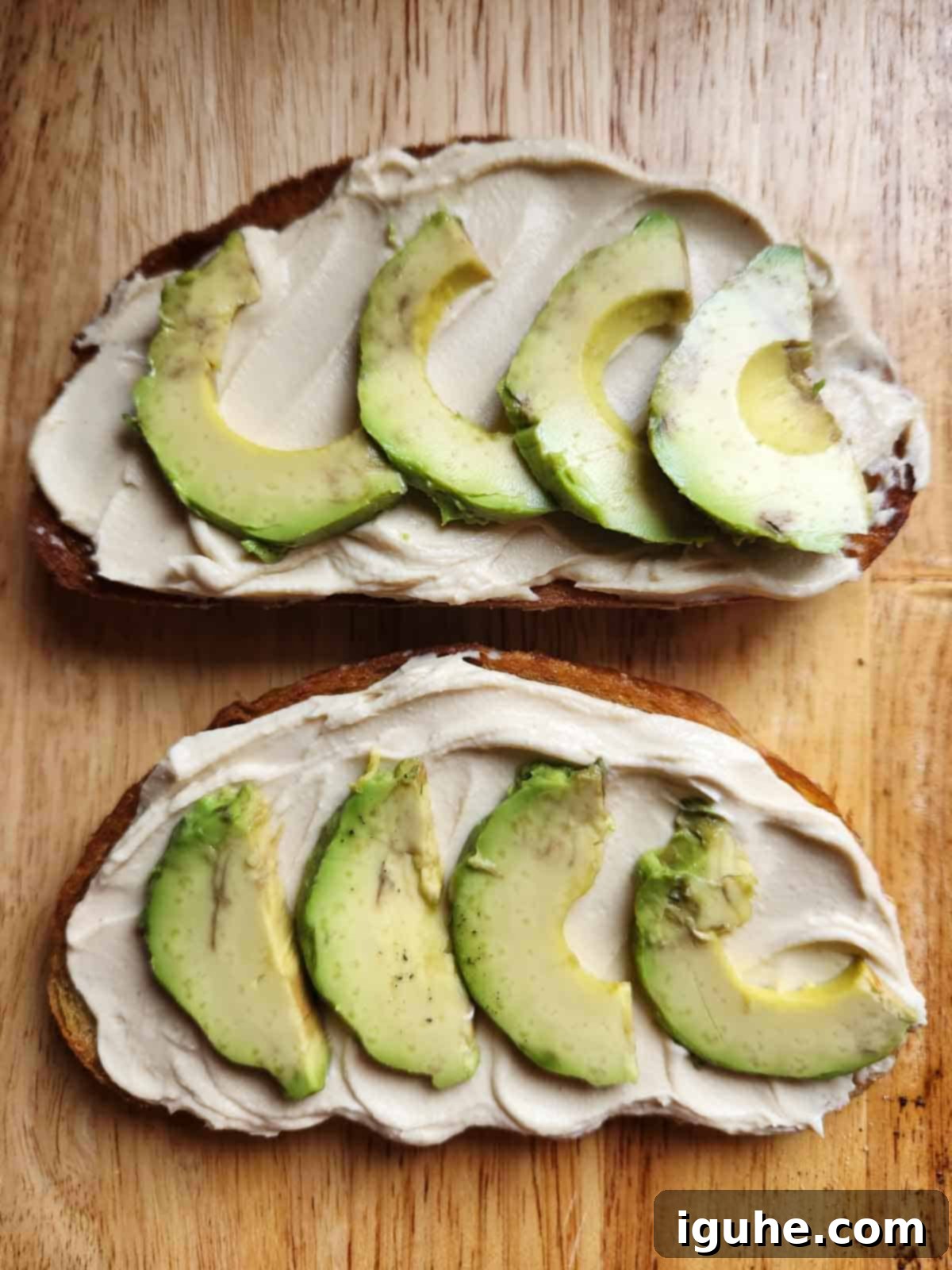 Two slices of toast topped with creamy hummus and slices of fresh avocado, ready for the final touches.