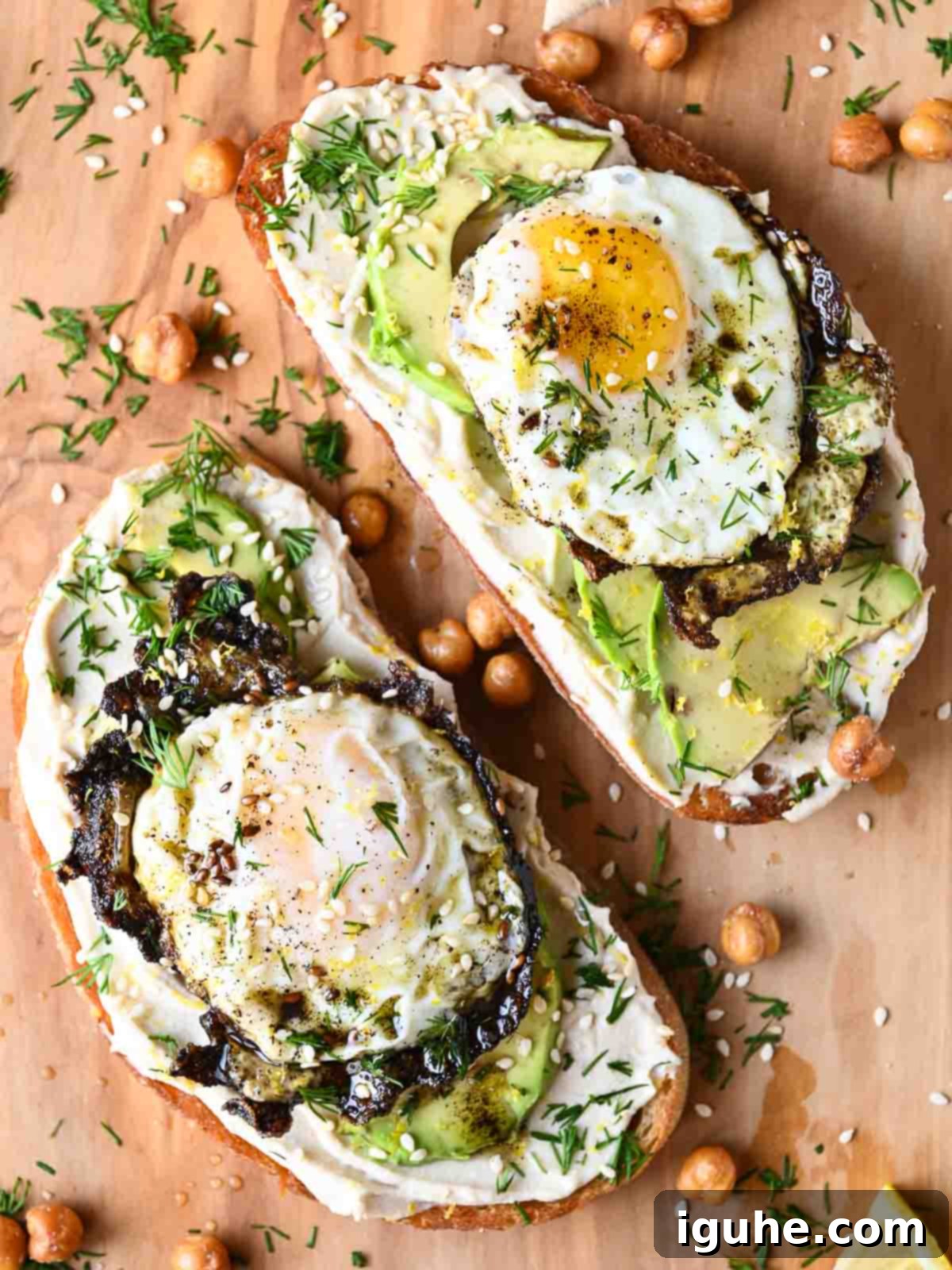 An overhead shot of delicious hummus toast on a wooden cutting board, topped with perfectly fried za'atar eggs and slices of creamy avocado.