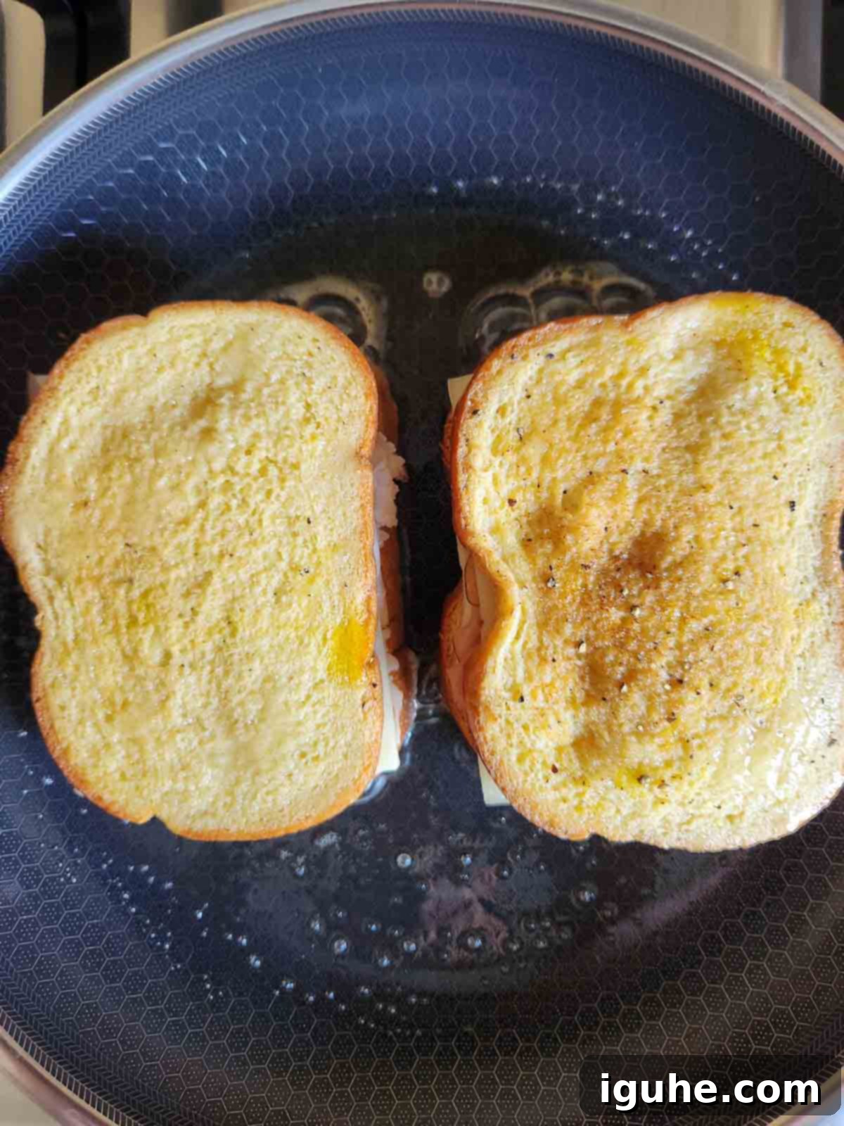 Overhead view of two Monte Cristo sandwiches cooking in a frying pan with melted butter.