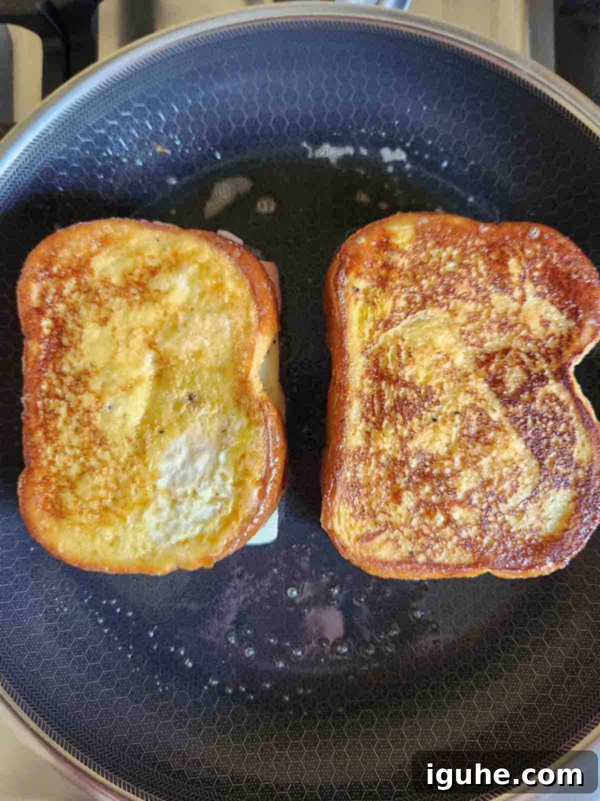 Golden-brown Monte Cristo sandwiches cooking in a frying pan with butter and melted cheese.