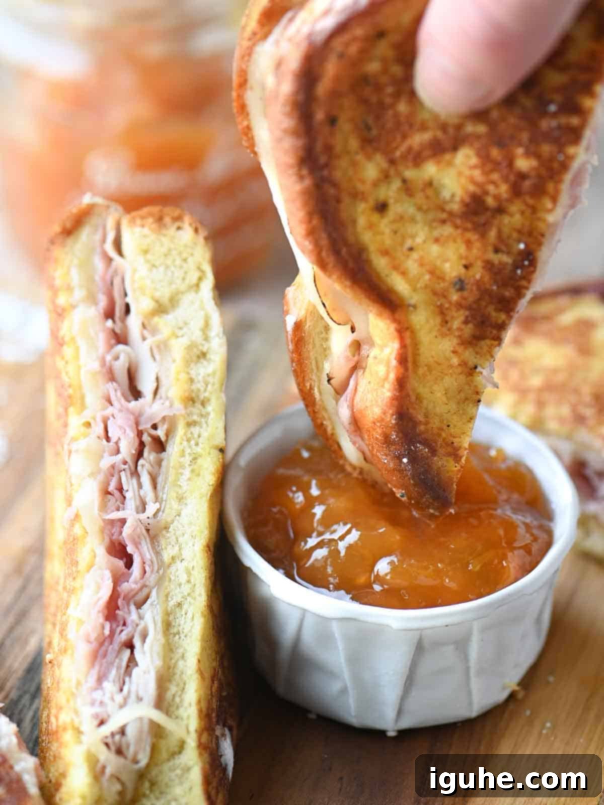 Close up of a Monte Cristo sandwich being dunked into apricot jam for a sweet and savory bite.